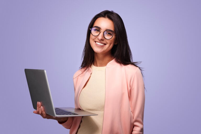 Jeune femme indépendante souriante debout dans un studio avec un ordinateur portable à la main