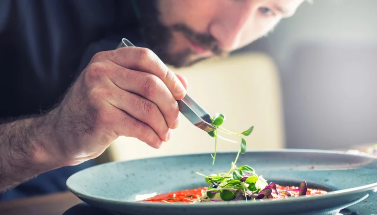 Chef en pleine création culinaire, ajoutant les touches finales à un plat raffiné. Découvrez l'art de la gastronomie dans un restaurant d'exception.