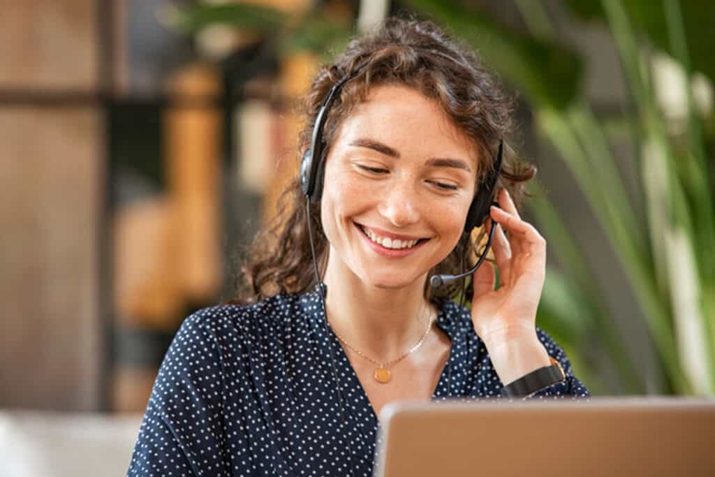 Femme en train de sourire parlant au client sur son ordinateur avec des écouteurs