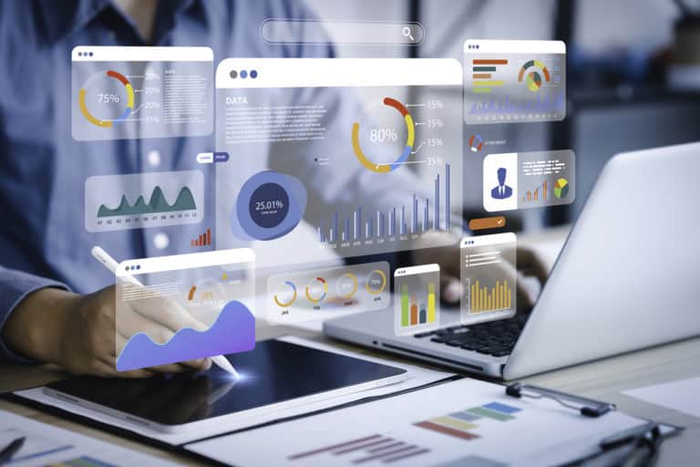 Image montrant une personne utilisant une tablette et un ordinateur portable pour analyser des données. Des graphiques et des tableaux de bord virtuels sont superposés sur l'image, affichant divers types de visualisations de données telles que des graphiques circulaires, des graphiques en barres et des courbes de tendance. Les graphiques montrent des pourcentages, des statistiques mensuelles et des données démographiques, symbolisant l'analyse et le suivi mensuel des performances.