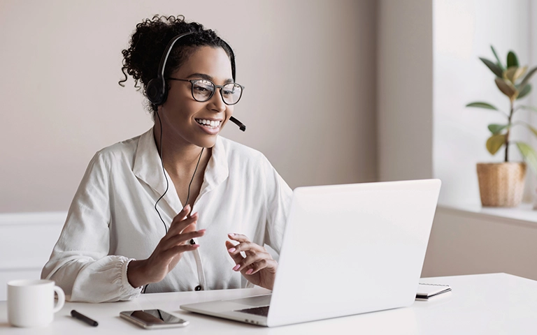 Femme souriante portant un casque avec micro, travaillant sur un ordinateur portable dans un environnement professionnel, illustrant un service d'accompagnement ou de support client pour un site web.