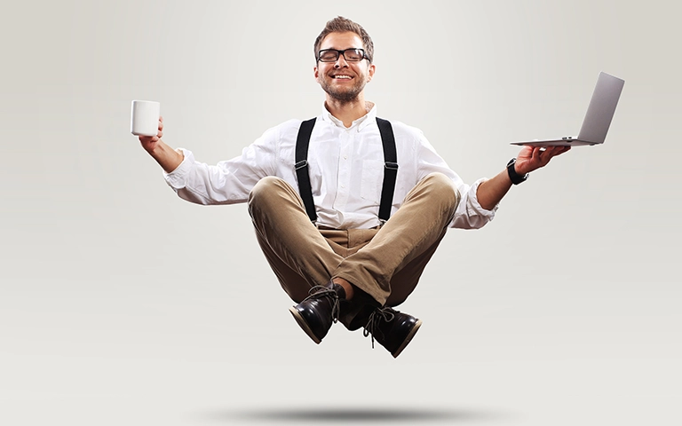 Homme souriant en position assise flottante, tenant une tasse dans une main et un ordinateur portable dans l'autre, symbolisant l'équilibre entre travail et détente, ou la facilité de gestion du contenu numérique.