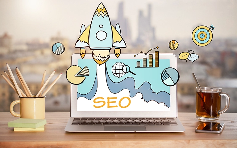 Image illustrant le concept du SEO. Un ordinateur portable affichant une fusée décollant, entourée d'icônes de graphiques, cibles et réseaux, symbolisant la croissance du référencement SEO. L'acronyme 'SEO' est inscrit en lettres orange sur l'écran. Des éléments de bureau comme des crayons et une tasse de thé sont placés autour, avec une vue floue d'une ville en arrière-plan.